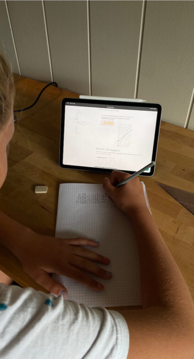 En student løser matematikkoppgaver på rutepapir med eBoken åpen på et nettbrett
